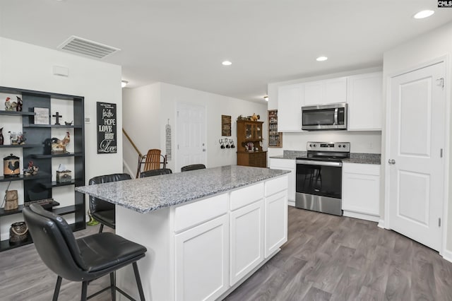 kitchen featuring visible vents, wood finished floors, appliances with stainless steel finishes, a breakfast bar area, and white cabinets