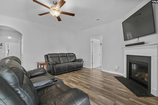 living room featuring visible vents, a fireplace with flush hearth, wood finished floors, arched walkways, and ceiling fan