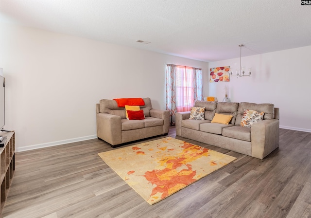 living room featuring a textured ceiling, visible vents, baseboards, wood finished floors, and an inviting chandelier