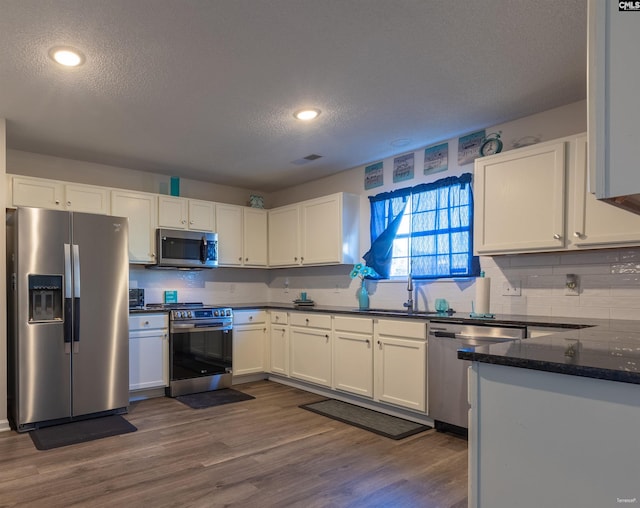 kitchen with white cabinetry, tasteful backsplash, a textured ceiling, dark wood finished floors, and stainless steel appliances