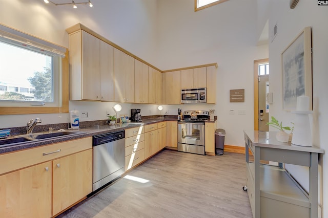 kitchen with a sink, light brown cabinetry, dark countertops, stainless steel appliances, and visible vents