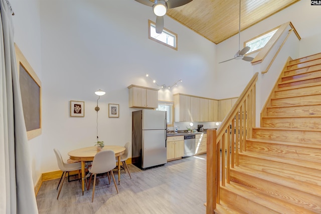 dining space featuring light wood-type flooring, a towering ceiling, stairway, and a ceiling fan