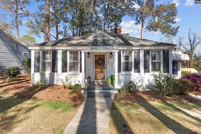 bungalow with a chimney, a front lawn, and brick siding