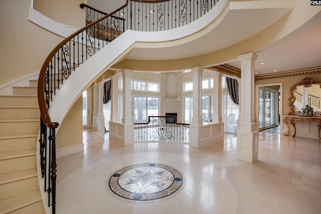entrance foyer featuring a decorative wall, a fireplace, a towering ceiling, stairway, and decorative columns