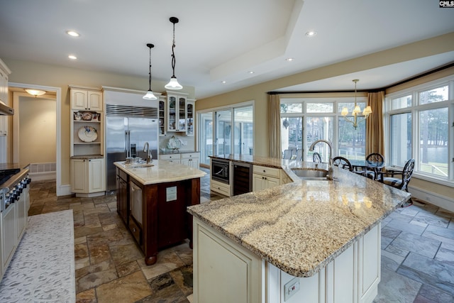 kitchen featuring stone tile floors, wine cooler, a sink, built in appliances, and a large island
