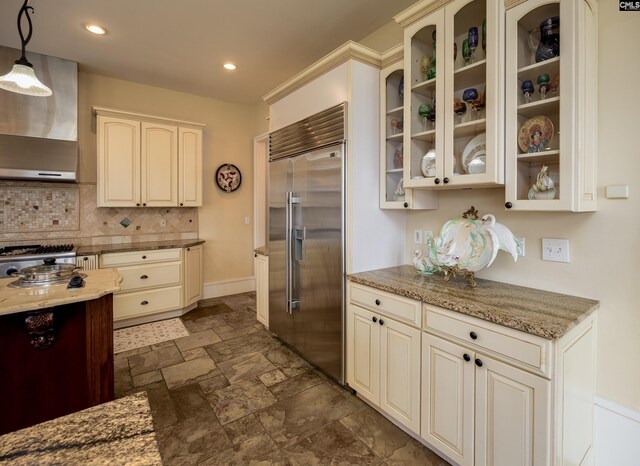 kitchen featuring wall chimney exhaust hood, cream cabinetry, stainless steel built in refrigerator, and backsplash