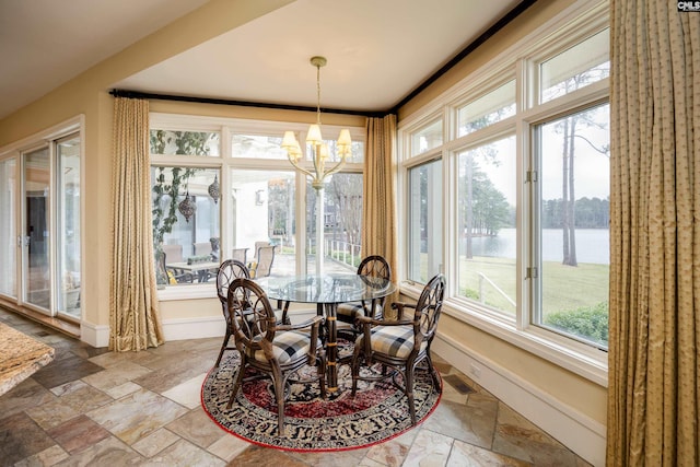 dining room featuring a water view, plenty of natural light, stone tile floors, and an inviting chandelier