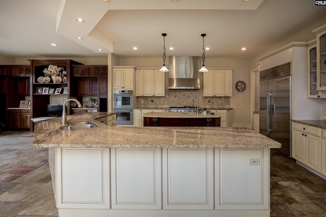 kitchen featuring stainless steel built in refrigerator, wall chimney exhaust hood, a sink, double oven, and a large island with sink
