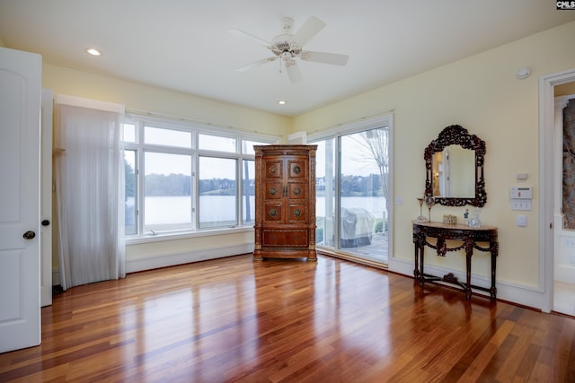 empty room with baseboards, a water view, wood finished floors, and a ceiling fan