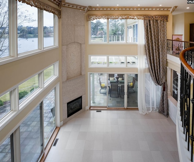 unfurnished living room featuring recessed lighting, a towering ceiling, visible vents, a glass covered fireplace, and light floors
