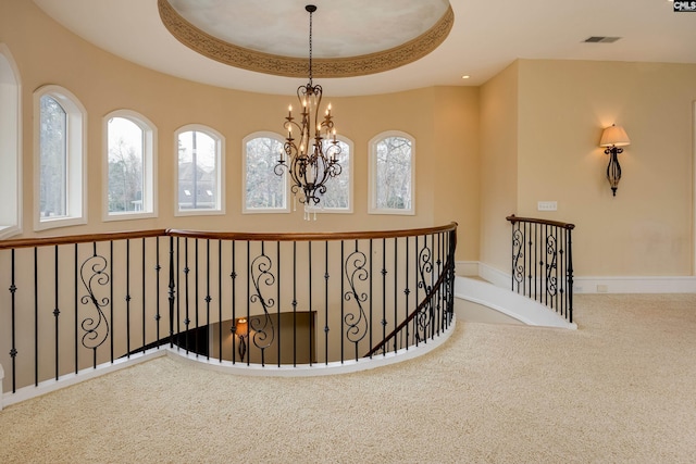 corridor featuring an upstairs landing, a tray ceiling, carpet floors, visible vents, and a notable chandelier