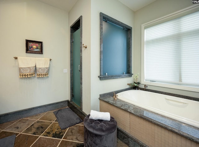 full bathroom with baseboards, a garden tub, and a shower stall