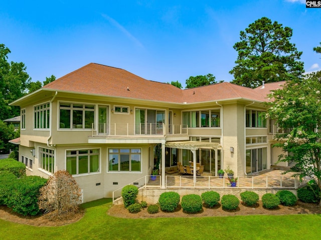 back of house featuring stucco siding, roof with shingles, a patio, a balcony, and a yard