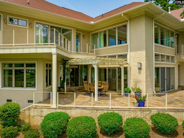 rear view of property with stucco siding, a balcony, brick siding, a pergola, and a patio area