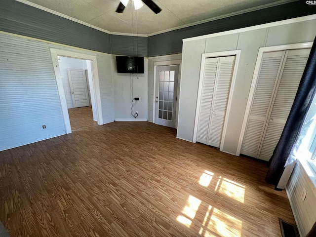 unfurnished bedroom featuring multiple closets, visible vents, ornamental molding, wood finished floors, and a ceiling fan