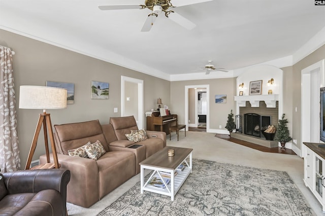 living room featuring a fireplace with raised hearth, baseboards, light colored carpet, and ceiling fan