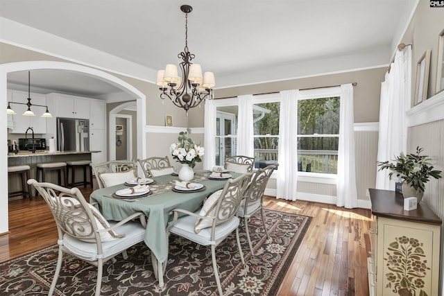 dining area with a notable chandelier, arched walkways, and hardwood / wood-style flooring