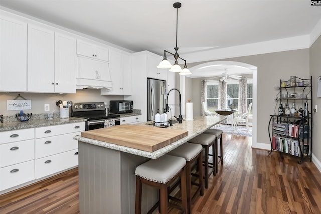 kitchen with dark wood-style flooring, premium range hood, appliances with stainless steel finishes, arched walkways, and white cabinetry
