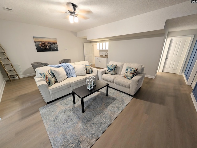 living room featuring baseboards, a textured ceiling, a ceiling fan, visible vents, and wood finished floors