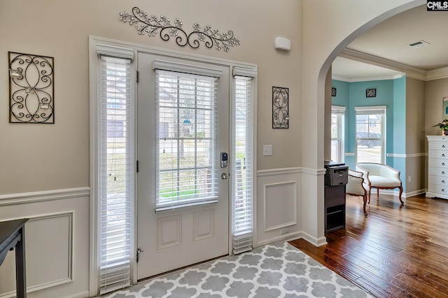 foyer entrance with arched walkways, visible vents, dark wood-type flooring, and crown molding