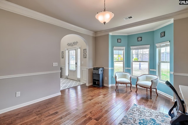 sitting room with arched walkways, visible vents, crown molding, and wood finished floors