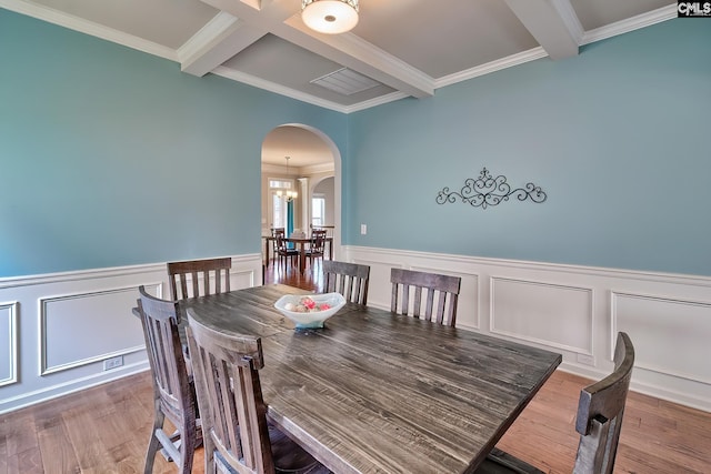 dining space featuring a wainscoted wall, wood finished floors, arched walkways, and beam ceiling