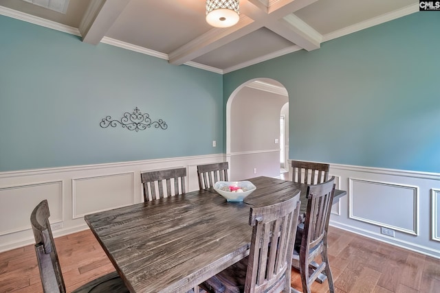 dining space featuring a wainscoted wall, arched walkways, beam ceiling, and wood finished floors