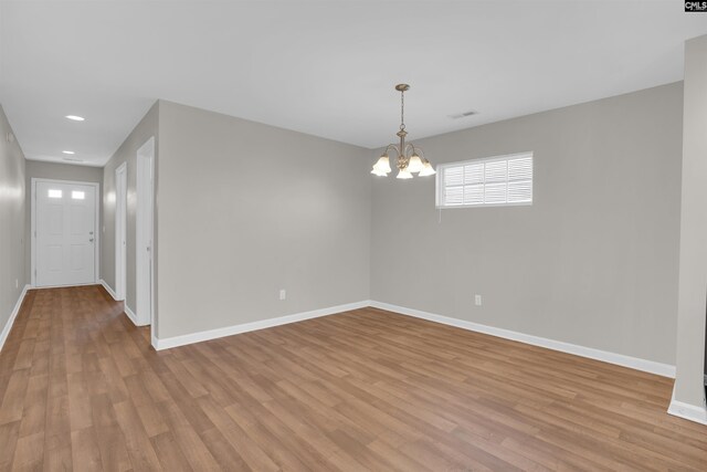 unfurnished room featuring baseboards, visible vents, light wood-style floors, and a notable chandelier