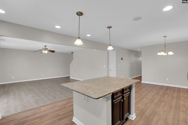 kitchen featuring open floor plan, light wood-style flooring, ceiling fan with notable chandelier, and pendant lighting