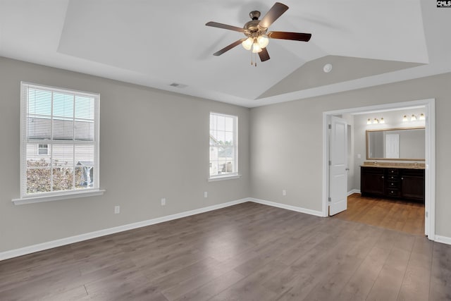 unfurnished bedroom with connected bathroom, vaulted ceiling, wood finished floors, baseboards, and visible vents