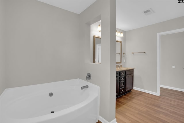 bathroom with vanity, a bath, baseboards, visible vents, and wood finished floors
