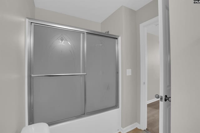 bathroom with baseboards, bath / shower combo with glass door, and wood finished floors