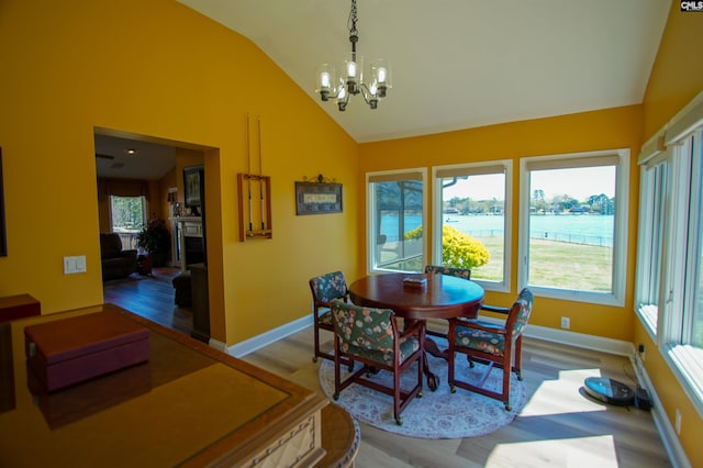 dining area with an inviting chandelier, a water view, vaulted ceiling, and wood finished floors