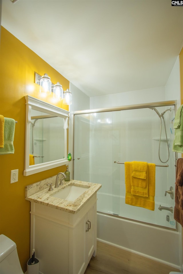 bathroom featuring combined bath / shower with glass door, wood finished floors, toilet, and vanity