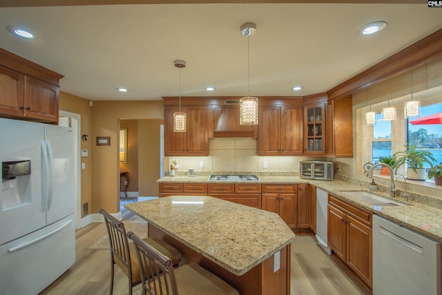kitchen featuring stainless steel gas stovetop, white fridge with ice dispenser, premium range hood, a sink, and dishwashing machine