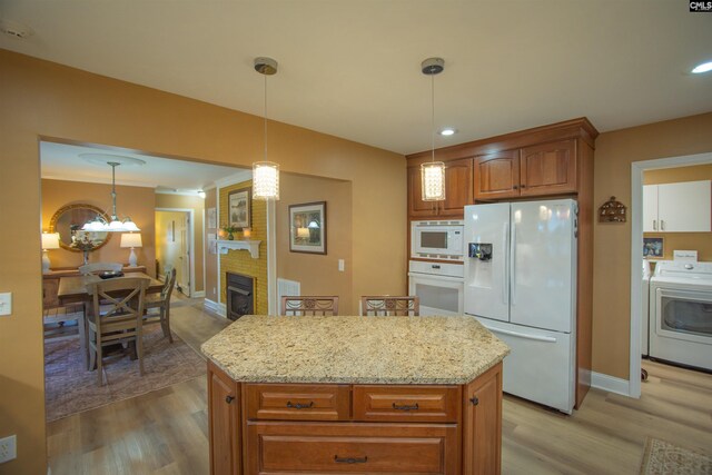 kitchen with white appliances, washer / clothes dryer, brown cabinets, light wood-style floors, and a center island