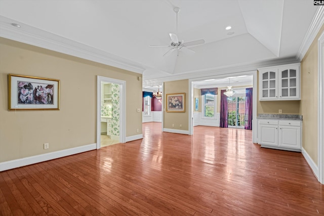 unfurnished living room featuring ornamental molding, ceiling fan with notable chandelier, a tray ceiling, and light wood-type flooring
