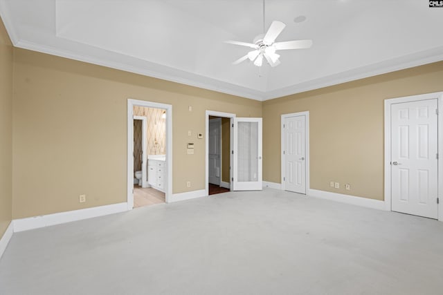unfurnished bedroom with two closets, a tray ceiling, baseboards, ensuite bath, and light carpet