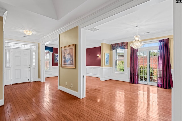 entryway with crown molding, an inviting chandelier, wood-type flooring, visible vents, and wainscoting