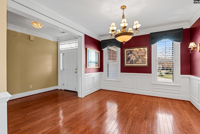 unfurnished dining area with an inviting chandelier, hardwood / wood-style floors, ornamental molding, and wainscoting