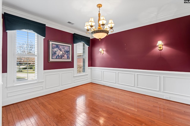 empty room featuring an inviting chandelier, wainscoting, hardwood / wood-style flooring, and visible vents