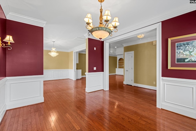 empty room featuring an inviting chandelier, a wainscoted wall, ornamental molding, and wood-type flooring