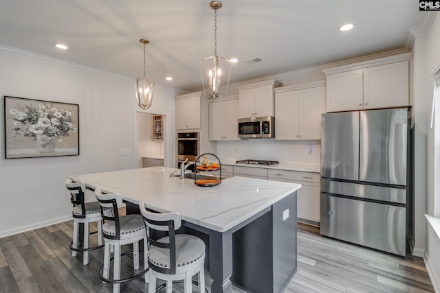 kitchen featuring an island with sink, crown molding, tasteful backsplash, appliances with stainless steel finishes, and light wood-style floors