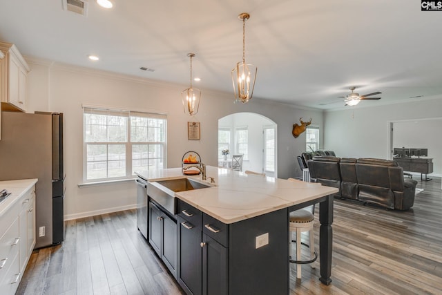 kitchen featuring a kitchen bar, stainless steel appliances, a sink, arched walkways, and visible vents