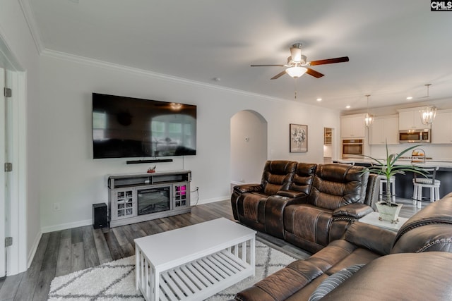 living room with crown molding, wood finished floors, baseboards, arched walkways, and ceiling fan