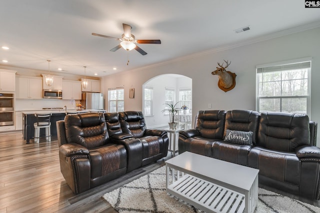living area with crown molding, arched walkways, visible vents, a ceiling fan, and wood finished floors