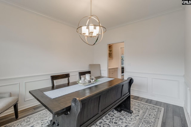 dining room with ornamental molding, a wainscoted wall, a notable chandelier, and wood finished floors