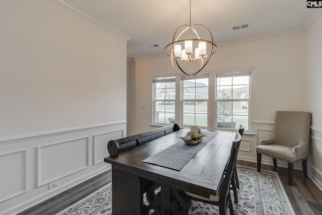 dining area with a wainscoted wall, crown molding, dark wood-style floors, visible vents, and an inviting chandelier