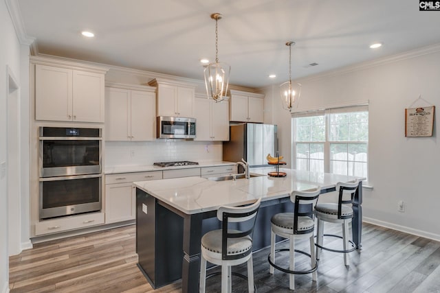 kitchen with ornamental molding, stainless steel appliances, decorative backsplash, a center island with sink, and light wood-style flooring