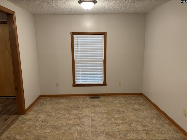 empty room featuring baseboards, a textured ceiling, and visible vents